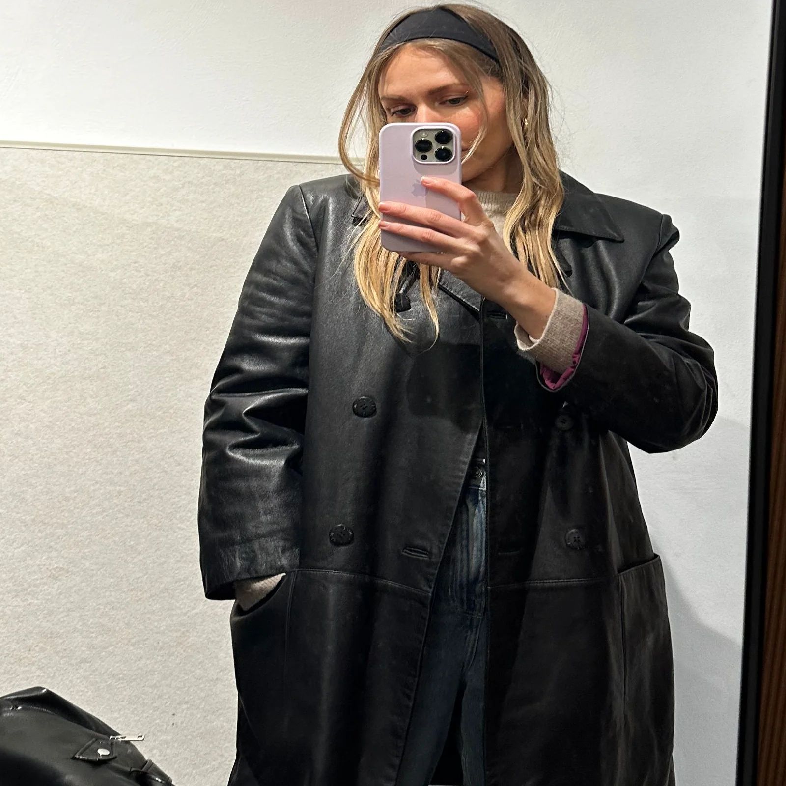 Dena trying on a mid-length black vintage leather coat with wide-leg jeans in the fitting room at ENSŌ Vintage, Amsterdam