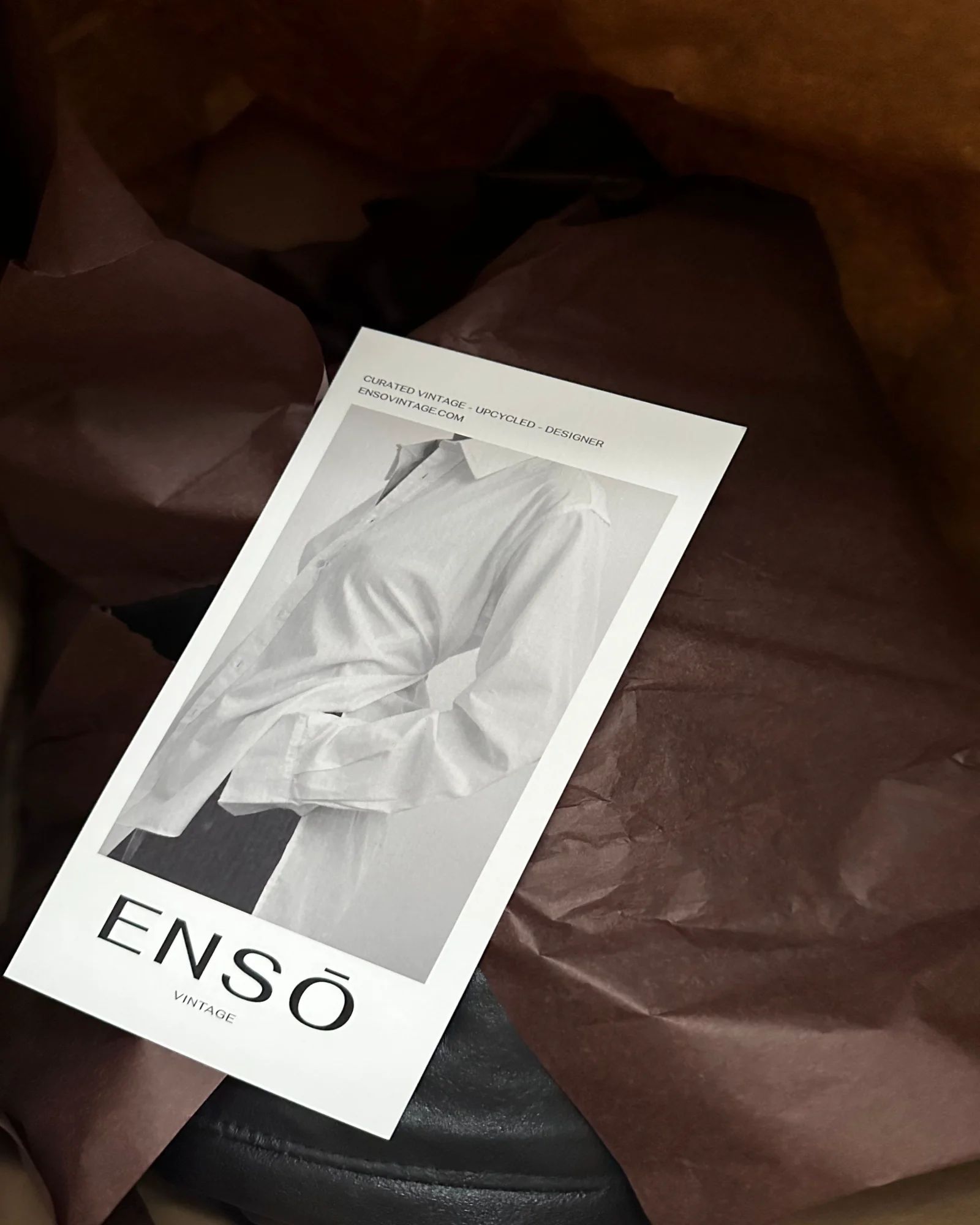 ENSŌ Vintage flyer on brown tissue paper in a shopping bag, with a black leather coat just visible underneath